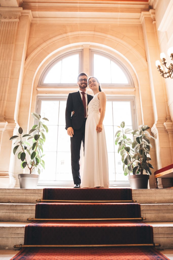 Couple de mariés de profil devant une fenêtre lumineuse avec plantes vertes, photo de mariage