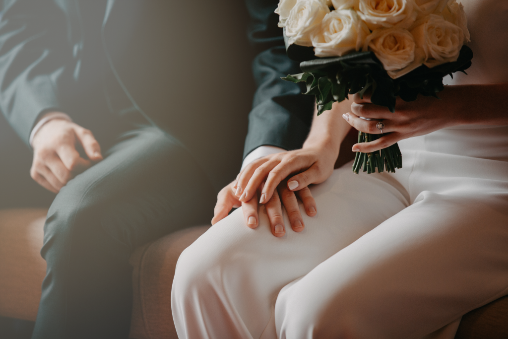 Gros plan de mains de mariés entrelacées avec alliance et bouquet, séance photo mariage