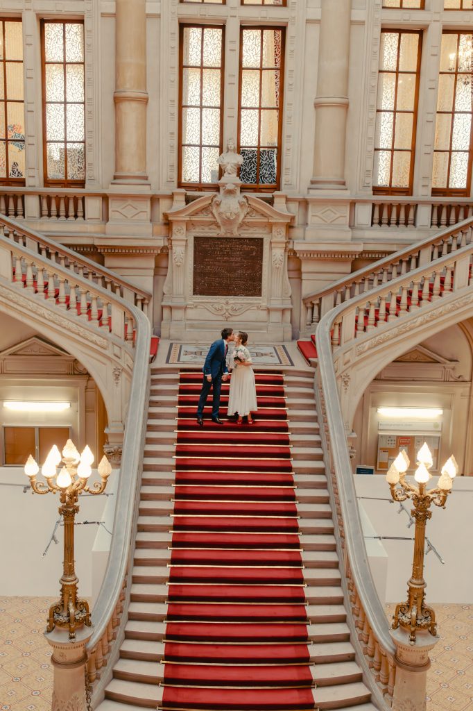 Couple de mariés posant sur un grand escalier rouge dans une salle de réception luxueuse, photo mariage