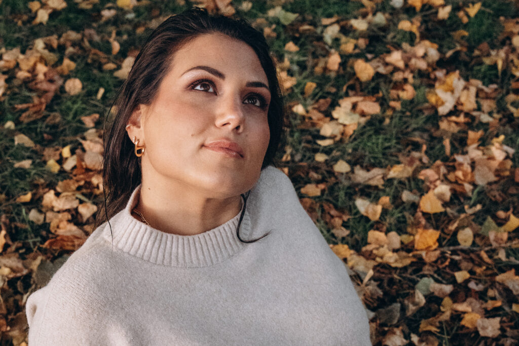 Femme allongée sur des feuilles d'automne souriante, portrait lifestyle en plein air